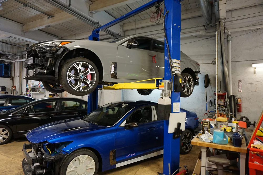 Auto body technician inspecting pothole damage under a car's front bumper at a Philadelphia collision shop